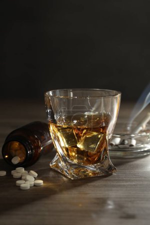Alcohol addiction. Whiskey in glass, pills and cigarettes on wooden table