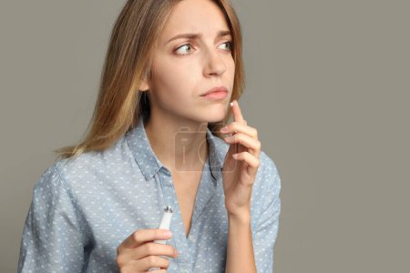 Mujer con herpes aplicando crema sobre el labio sobre fondo gris claro