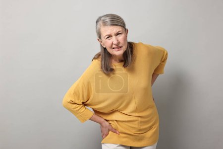 Symptome einer Arthritis. Frau leidet unter Rückenschmerzen auf grauem Hintergrund