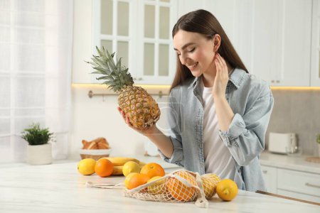 Téléchargez les photos : Femme avec ananas et sac à ficelle de fruits frais à table en marbre clair dans la cuisine - en image libre de droit