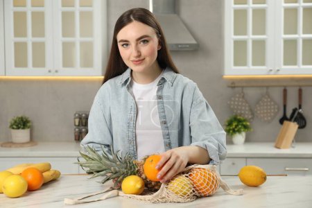 Téléchargez les photos : Femme avec sac à ficelle de fruits frais à table en marbre clair dans la cuisine - en image libre de droit