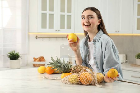 Téléchargez les photos : Femme avec citrons et sac à ficelle de fruits frais à table en marbre clair dans la cuisine - en image libre de droit