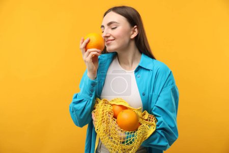 Téléchargez les photos : Femme avec sac à ficelle d'oranges fraîches sur fond orange - en image libre de droit