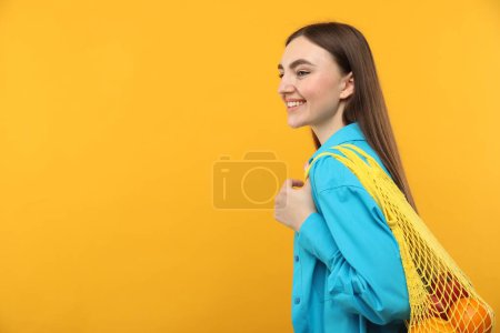 Téléchargez les photos : Femme avec sac à ficelle d'oranges fraîches sur fond orange, espace pour le texte - en image libre de droit