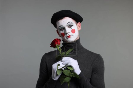 Portrait of mime artist with red rose on grey background