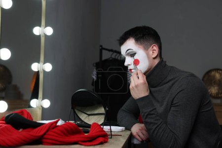 Joven aplicando maquillaje de mimo cerca del espejo en el vestidor