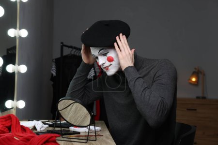 Mime artist putting on beret near mirror in dressing room