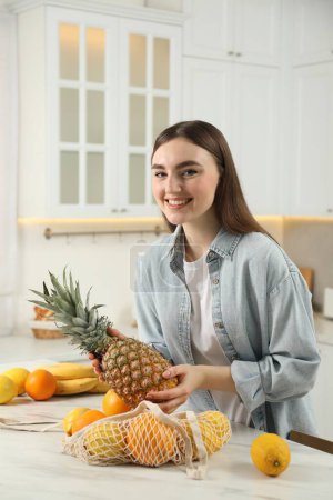 Téléchargez les photos : Femme sortant l'ananas du sac à ficelle à la table en marbre clair dans la cuisine - en image libre de droit