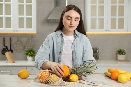 Téléchargez les photos : Femme avec sac à ficelle de fruits frais à table en marbre clair dans la cuisine - en image libre de droit