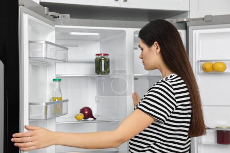 Mujer molesta cerca de refrigerador vacío en la cocina