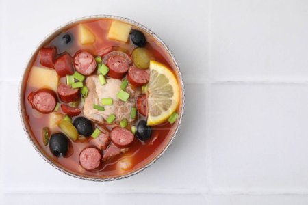 Téléchargez les photos : Soupe de viande solyanka avec de fines saucisses fumées sèches dans un bol sur une table carrelée blanche, vue sur le dessus. Espace pour le texte - en image libre de droit