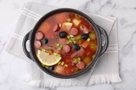 Meat solyanka soup with thin dry smoked sausages in bowl on white marble table, top view