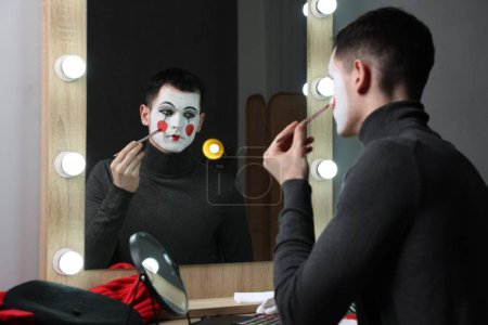 Junger Mann schminkt sich in Umkleidekabine neben Spiegel