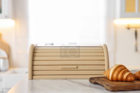Brotdose und Brett aus Holz mit Croissants auf weißem Marmortisch in der Küche