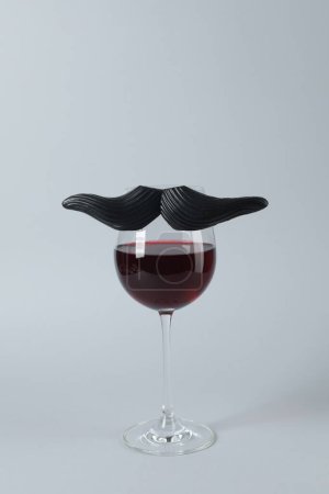 Téléchargez les photos : Verre de vin rouge avec drôle de fausse moustache sur fond gris - en image libre de droit