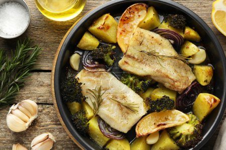 Foto de Trozos de delicioso bacalao al horno con verduras, limón y especias en plato sobre mesa de madera, puesta plana - Imagen libre de derechos