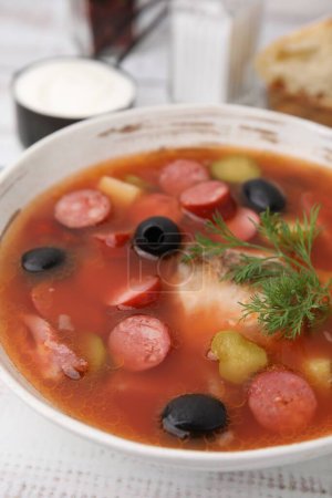 Téléchargez les photos : Soupe de viande solyanka avec de fines saucisses fumées sèches dans un bol sur une table blanche, gros plan - en image libre de droit