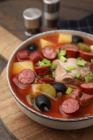 Téléchargez les photos : Soupe de viande solyanka avec de fines saucisses fumées sèches dans un bol sur une planche de bois, gros plan - en image libre de droit