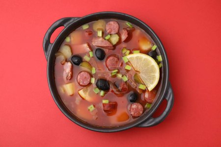 Téléchargez les photos : Soupe de viande solyanka avec de fines saucisses fumées sèches dans un bol sur fond rouge, vue sur le dessus - en image libre de droit