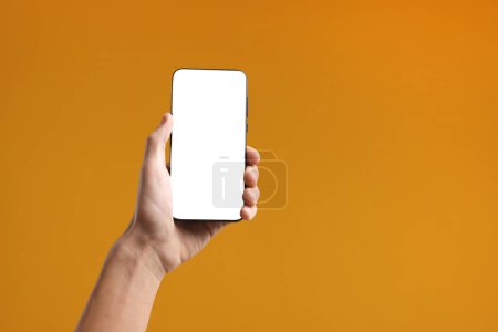 Mann hält Smartphone mit leerem Bildschirm auf orangefarbenem Hintergrund, Nahaufnahme. Mockup für Design