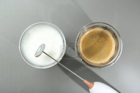 Mini mixer (milk frother), whipped milk and coffee in glasses on grey background, flat lay