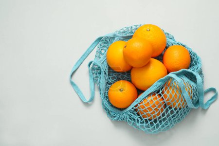 Téléchargez les photos : Sac à ficelle avec des oranges fraîches sur fond clair, vue de dessus. Espace pour le texte - en image libre de droit