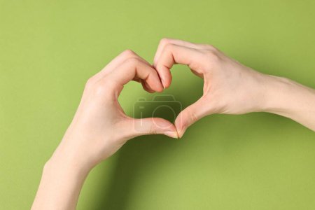 Woman showing heart gesture with hands on green background, closeup