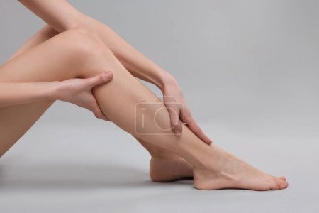 Woman suffering from leg pain on grey background, closeup