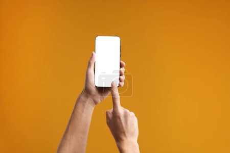 Mann mit Smartphone mit leerem Bildschirm auf orangefarbenem Hintergrund, Nahaufnahme. Mockup für Design