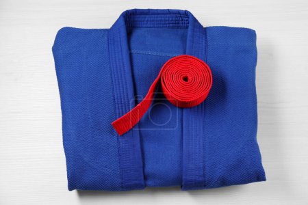 Red karate belt and blue kimono on wooden background, top view