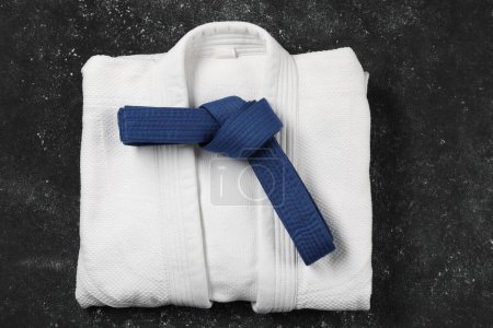 Blue karate belt and white kimono on gray textured background, top view