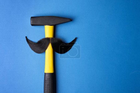Téléchargez les photos : Visage d'homme fait de moustache artificielle et marteau sur fond bleu, vue de dessus. Espace pour le texte - en image libre de droit