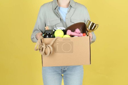 Frau hält Schachtel mit unerwünschten Dingen auf gelbem Hintergrund, Nahaufnahme