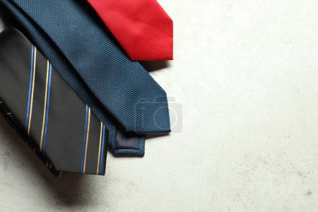 Different neckties on light textured table, flat lay. Space for text