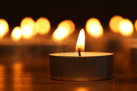 Burning tealight candle on dark surface, closeup