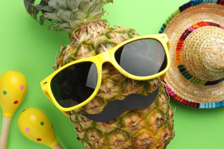 Téléchargez les photos : Chapeau sombrero mexicain, ananas avec lunettes de soleil, fausse moustache et maracas sur fond vert, plat - en image libre de droit