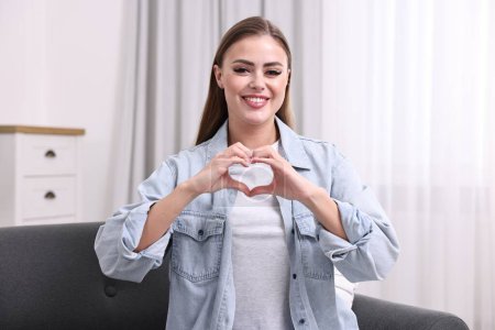 Glückliche Frau zeigt Herz-Geste mit Händen zu Hause