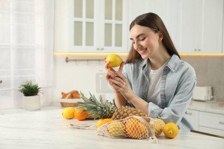 Téléchargez les photos : Femme avec citron et sac à ficelle de fruits frais à table en marbre clair dans la cuisine - en image libre de droit