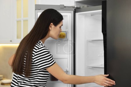 Mujer joven cerca de refrigerador vacío en la cocina
