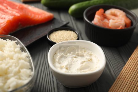 Téléchargez les photos : Fromage à la crème dans un bol et d'autres ingrédients pour les sushis sur une table en bois noir, gros plan - en image libre de droit