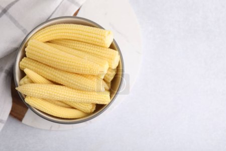 Tasty fresh yellow baby corns in bowl on white table, top view. Space for text