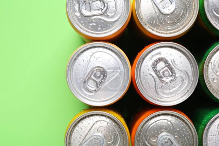 Bebidas energéticas en latas mojadas sobre fondo verde, vista superior. Espacio para texto