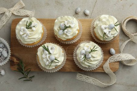 Tasty Easter cupcakes with vanilla cream, candies and ribbon on gray table, flat lay