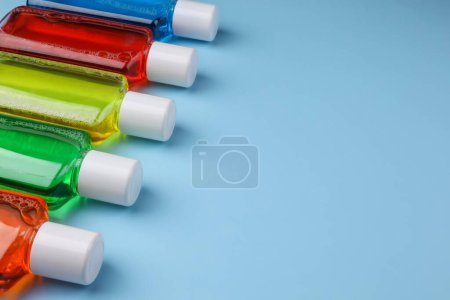 Fresh mouthwashes in bottles on light blue background, closeup. Space for text