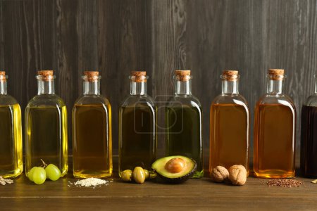 Foto de Grasas vegetales. Diferentes aceites en botellas de vidrio e ingredientes en mesa de madera - Imagen libre de derechos