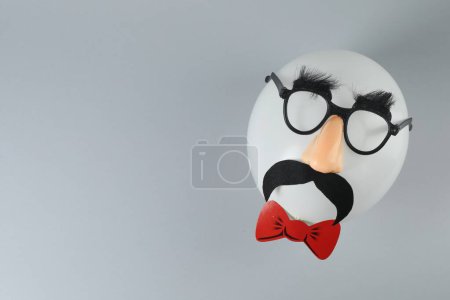 Téléchargez les photos : Visage d'homme en ballon, masque drôle avec fausse moustache, nez et lunettes sur fond gris, vue de dessus. Espace pour le texte - en image libre de droit