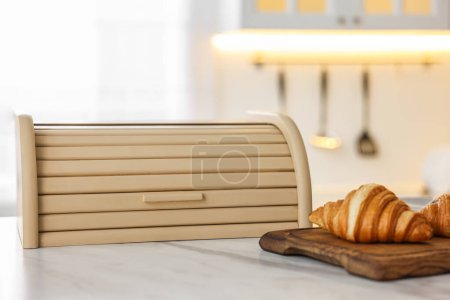 Brotdose und Brett aus Holz mit Croissants auf weißem Marmortisch in der Küche