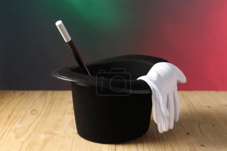 Sombrero de mago, varita y guantes sobre mesa de madera sobre fondo de color