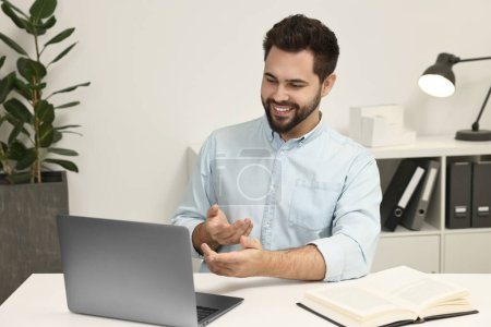 Foto de Hombre joven que tiene chat de vídeo a través de ordenador portátil en la mesa en el interior - Imagen libre de derechos