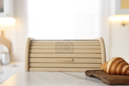 Wooden bread box and board with croissant on white marble table in kitchen